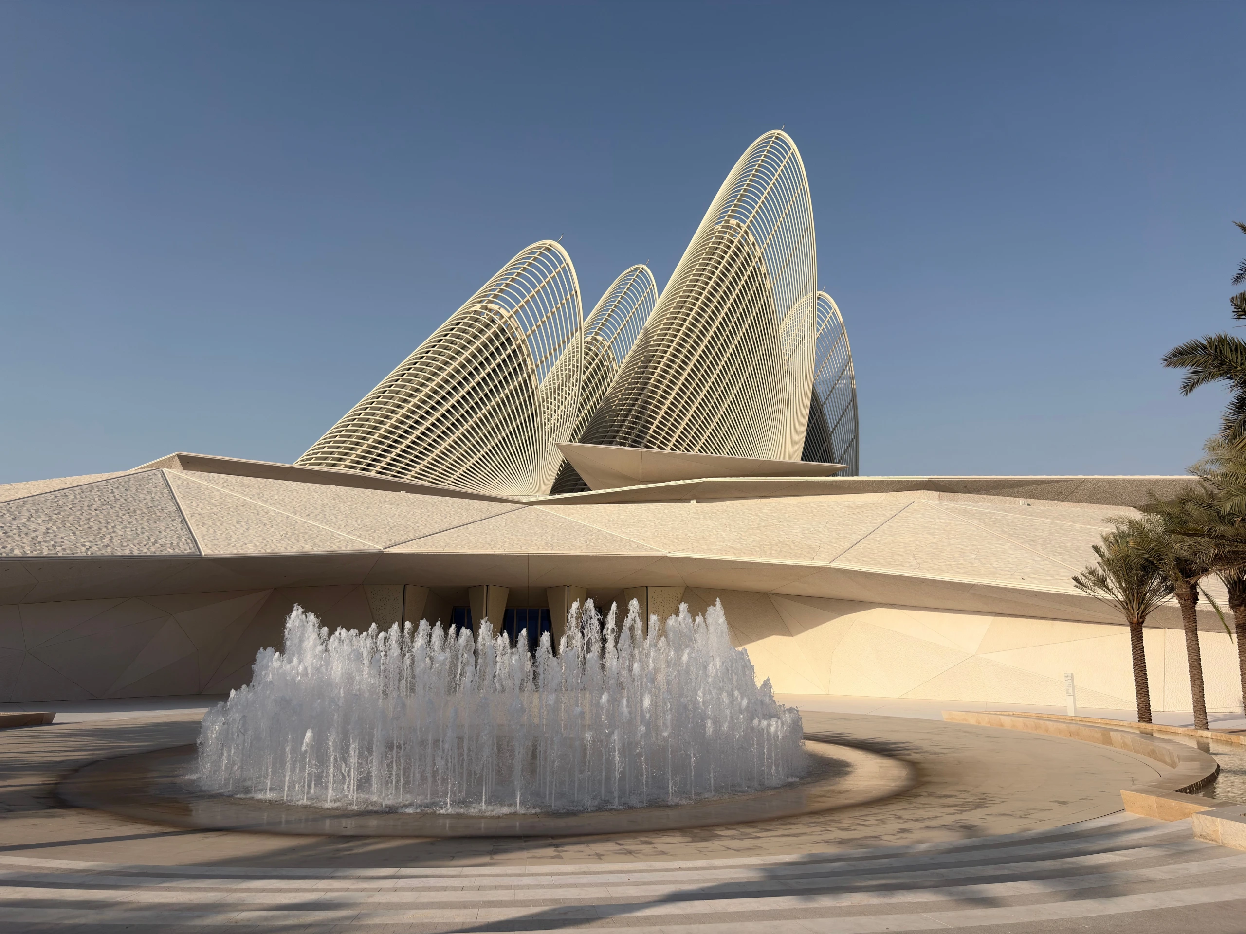Modern sculptural building with spires, a circular fountain, and palm trees in Abu Dhabi