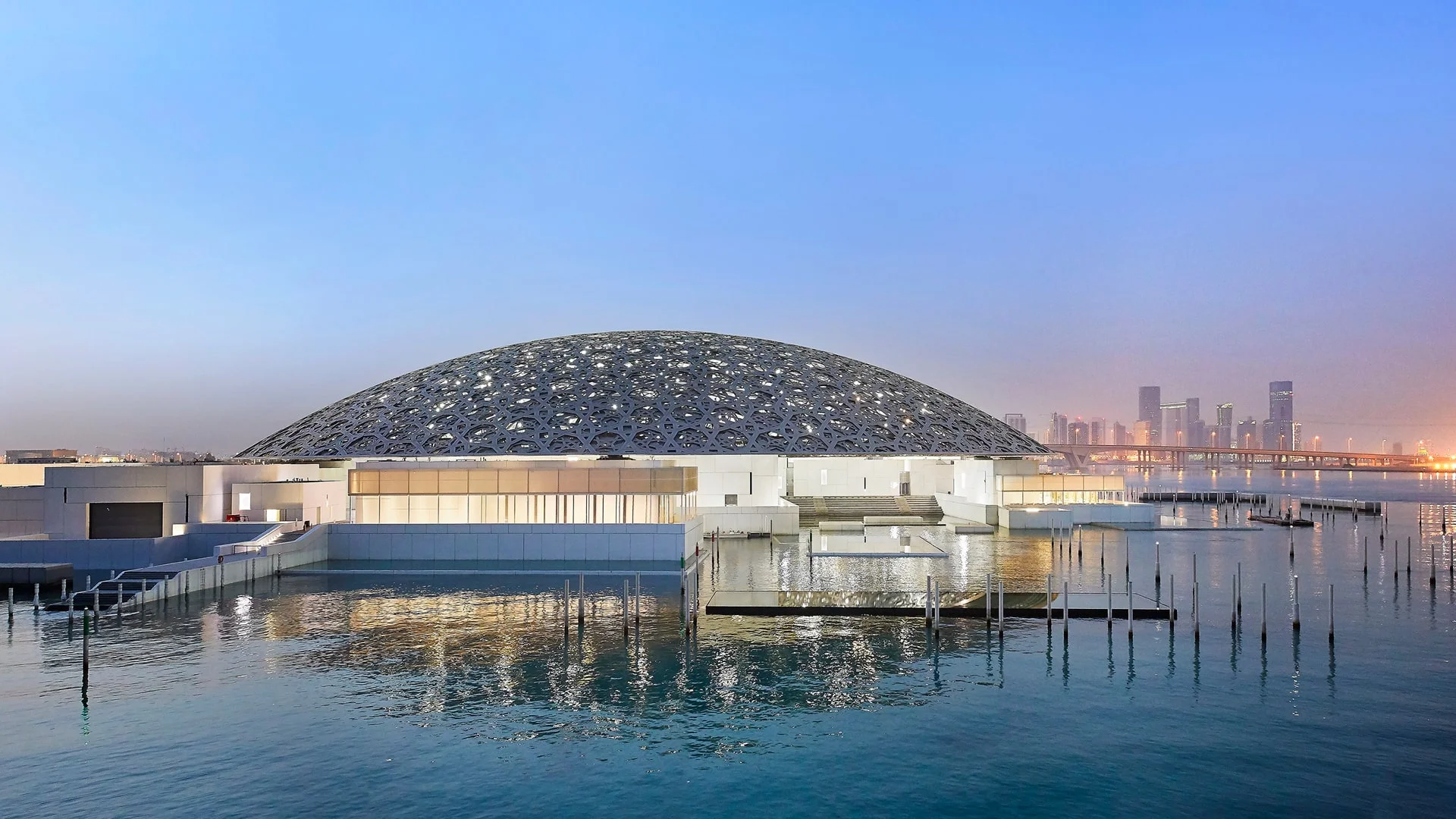 Louvre Abu Dhabi museum with intricate dome on calm water at dusk