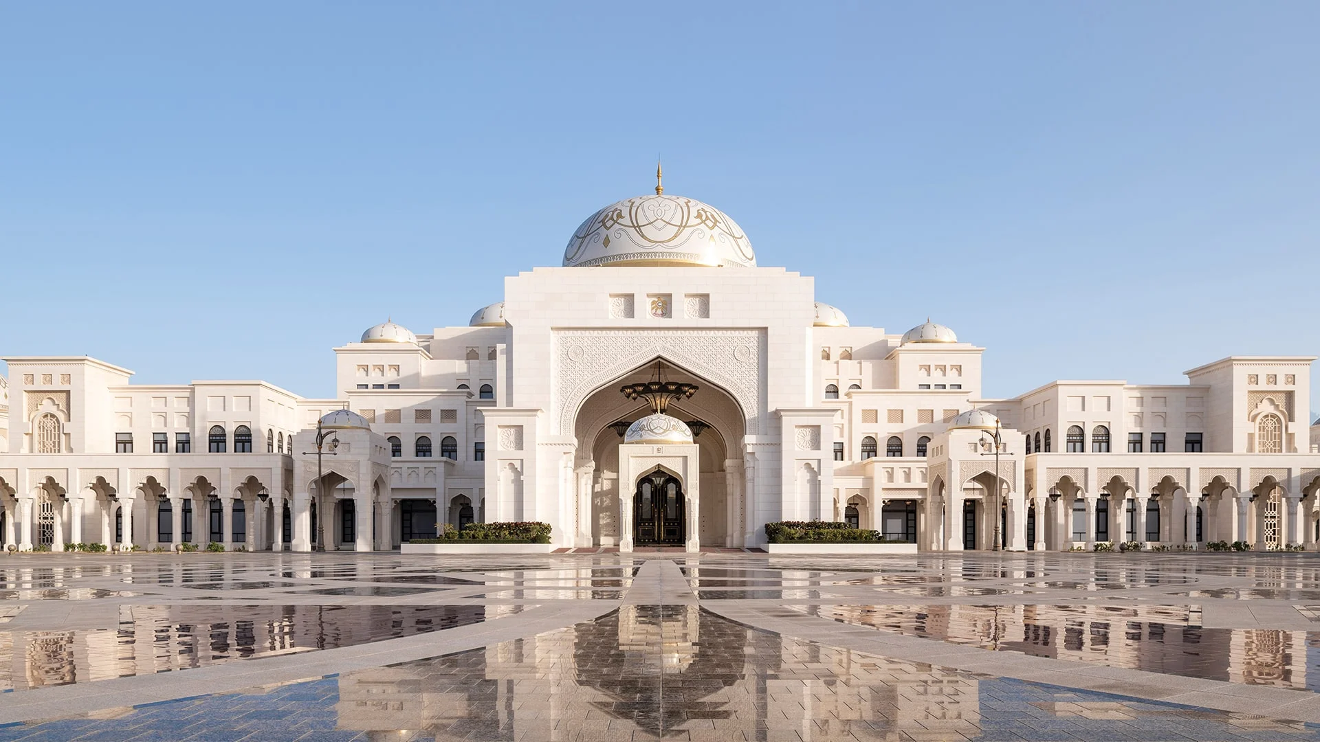 White palace with golden dome and arches, reflected on polished plaza under clear sky