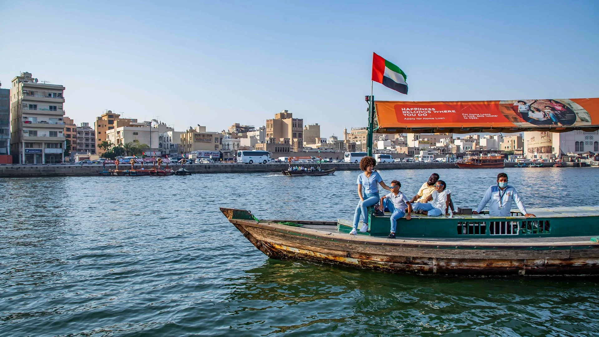 Tourists enjoy abra boat ride on Dubai Creek with city skyline behind