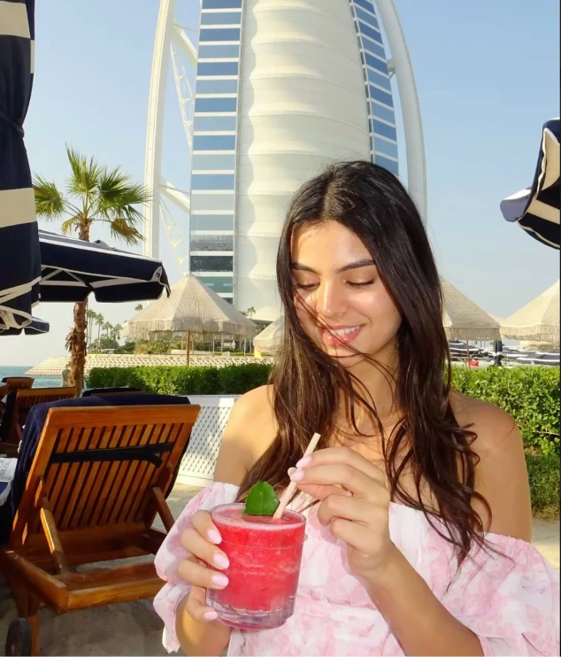 Woman with drink on beach with Burj Al Arab in background, Dubai