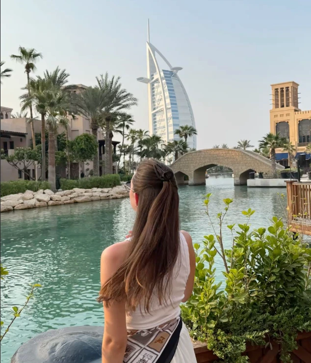 Woman views Burj Al Arab hotel and canal from lush gardens in Dubai