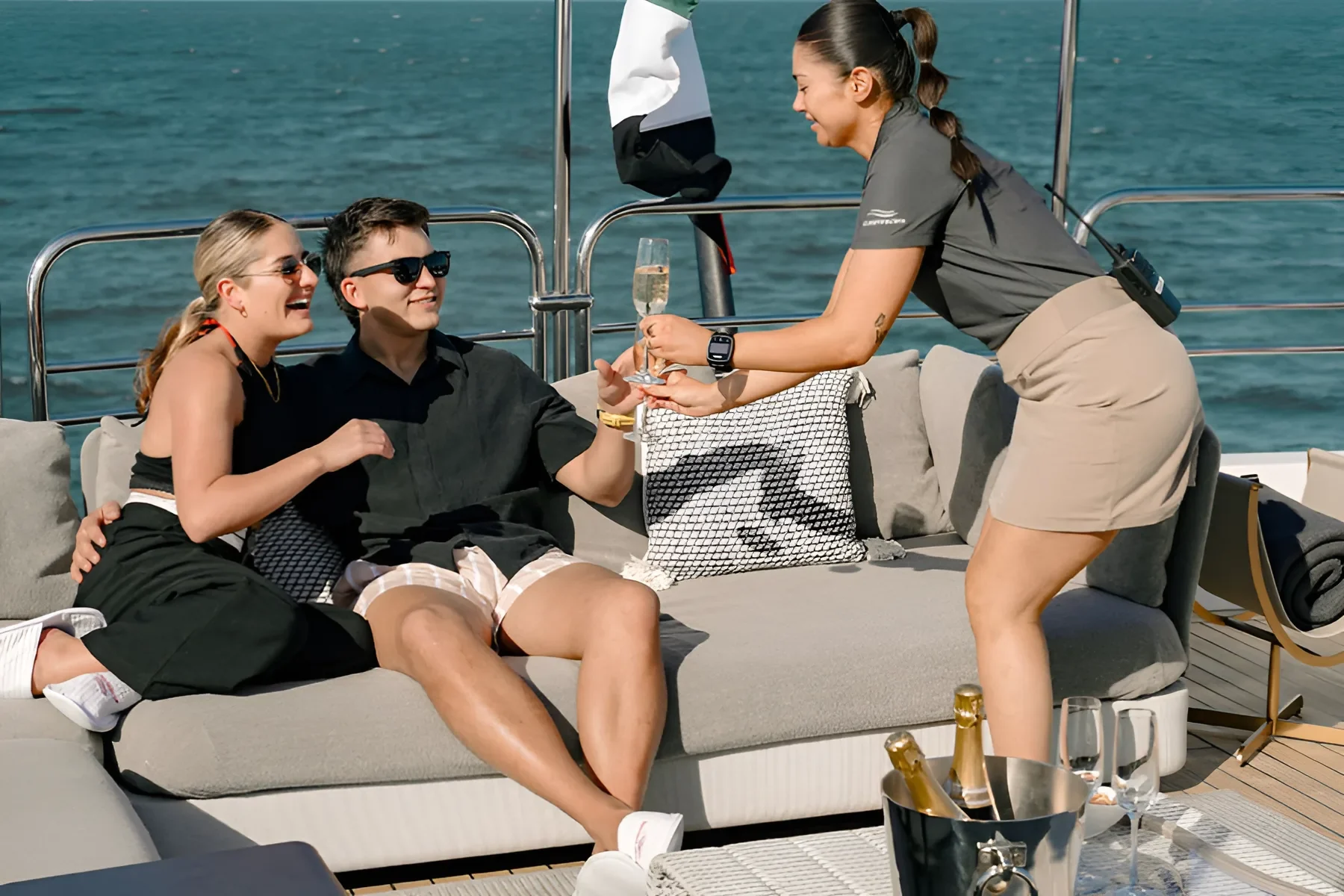 Yacht crew serves champagne to couple relaxing on deck of luxury yacht